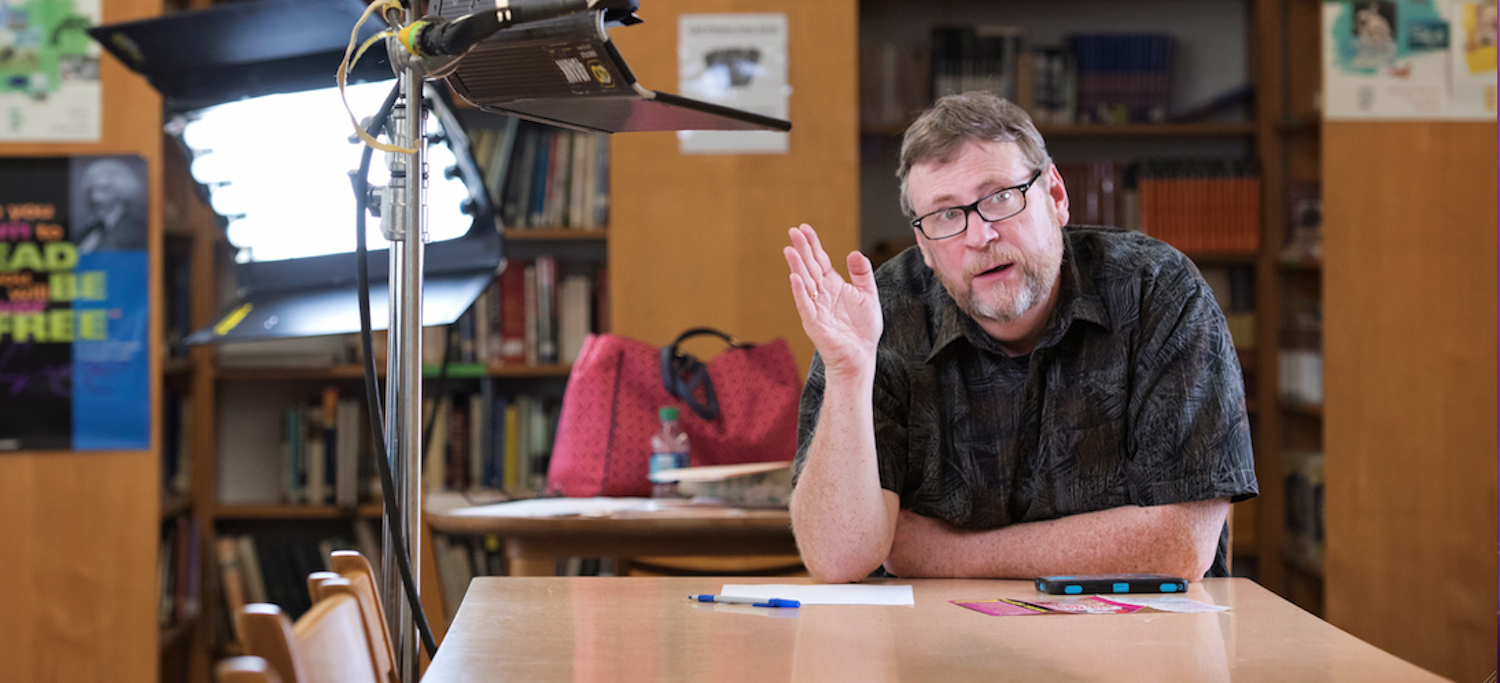 A man sitting at a table in front of a camera.