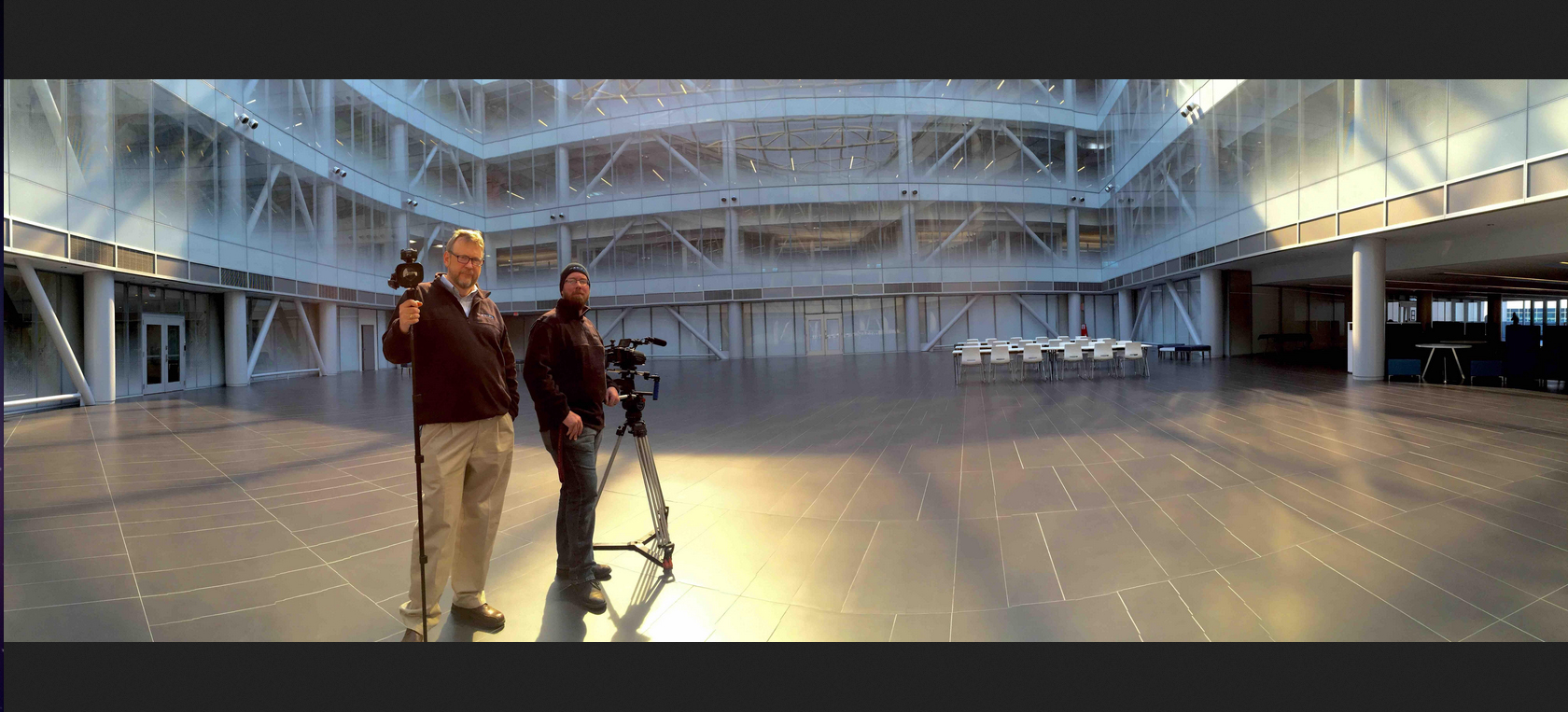 Two men standing in a large room with a camera.