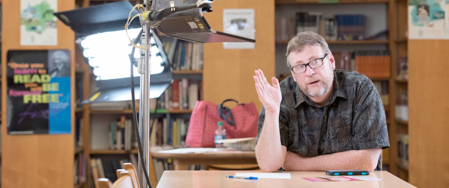 A man sitting at a table in front of a camera.