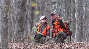 Two people in the woods with hunting gear on.